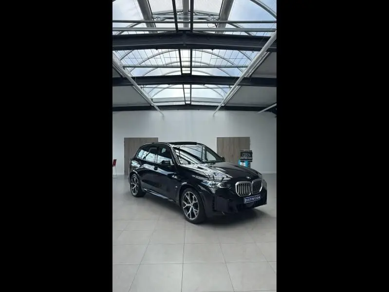 BMW X5 xDrive50e noir en 3/4 avant droit dans un showroom lumineux avec calandre chromée et jantes alliage.