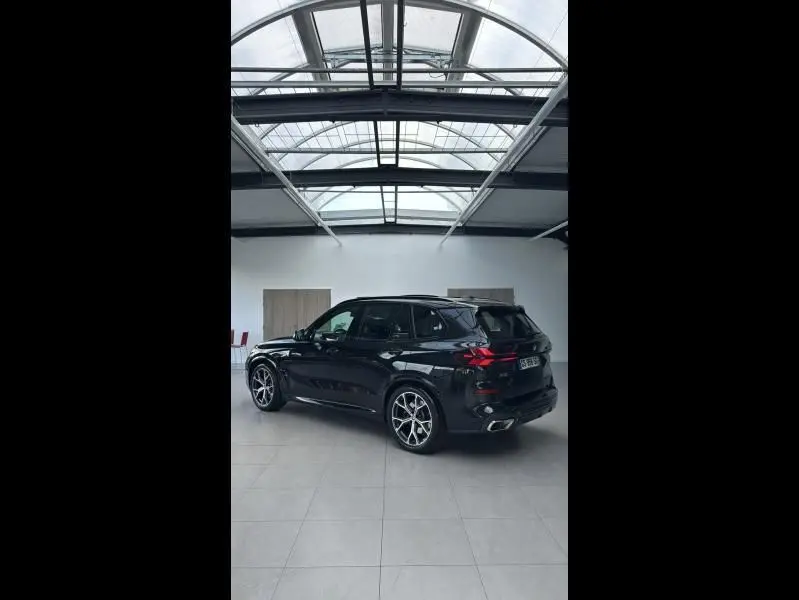 BMW X5 xDrive50e noir saphirschwarz en 3/4 arrière droit, avec jantes alliage 21'' style M Sport dans un showroom lumineux