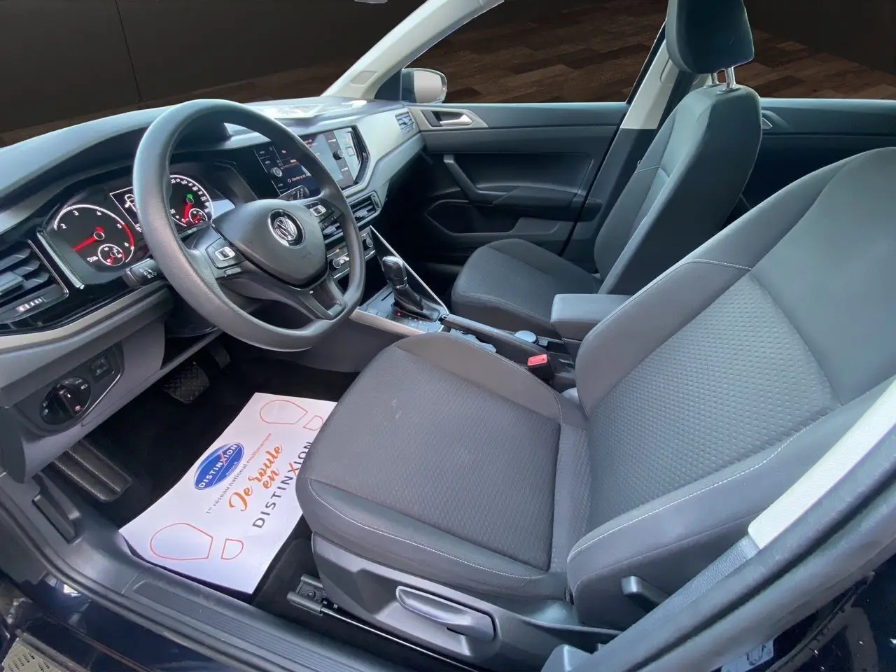 Vue intérieure côté conducteur de la Volkswagen Polo noire intense 2019, montrant sièges tissu noir et tableau de bord moderne.