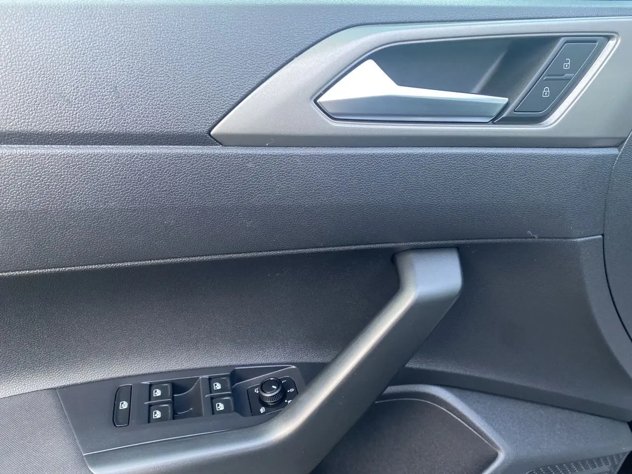 Détail de la porte côté conducteur d'une Volkswagen Polo noire, montrant les commandes des vitres et la poignée intérieure grise.