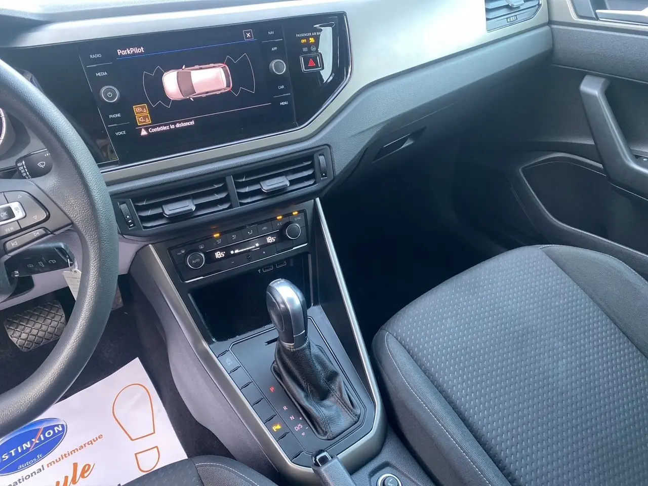 Vue intérieure centrée sur la console centrale et levier de vitesse d'une Volkswagen Polo noire avec écran tactile et sièges en tissu noir.