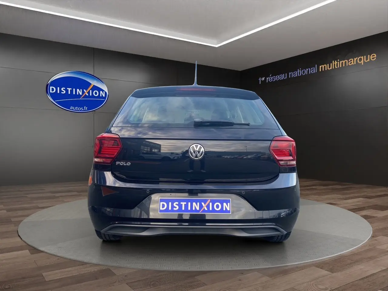 Vue arrière d'une Volkswagen Polo noire intense 2019 avec feux arrière rouges et logo VW visible sur un podium showroom.