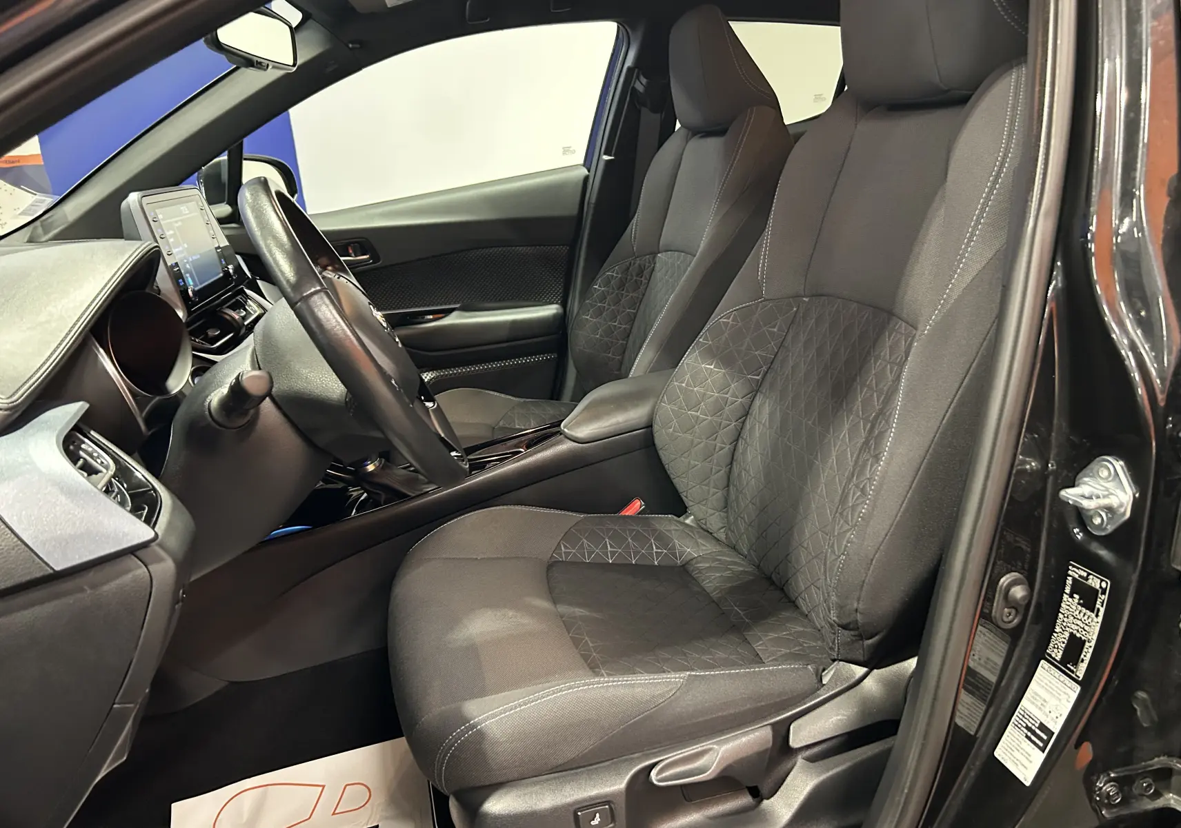 Vue intérieure côté conducteur du Toyota C-HR Hybride noir métal 2021, sièges tissu avec motifs géométriques et tableau de bord moderne.
