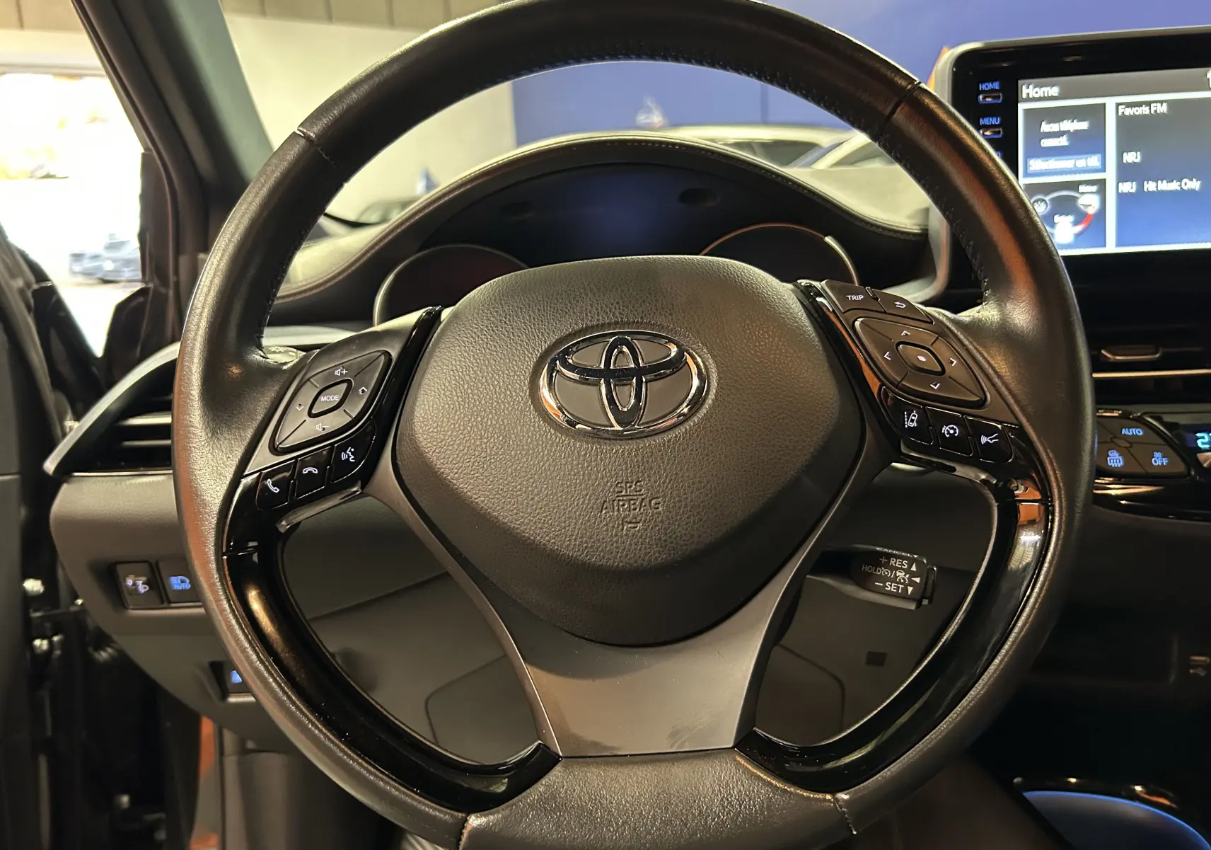 Volant noir du Toyota C-HR Hybride 122h Edition 2WD, avec commandes intégrées et tableau de bord numérique visible.