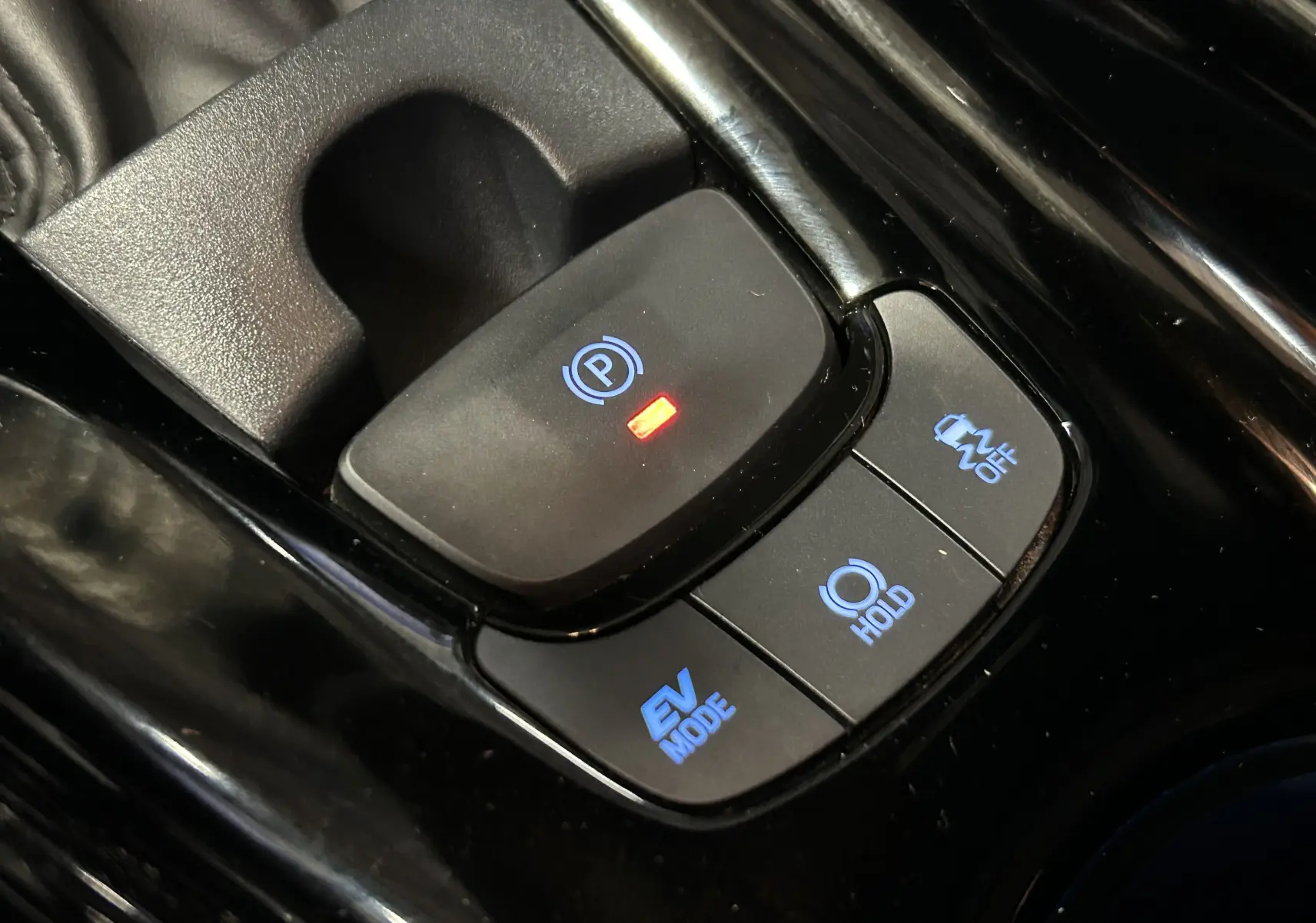 Gros plan sur les commandes de frein à main électronique et modes de conduite du Toyota C-HR Hybride noir métal 2021.