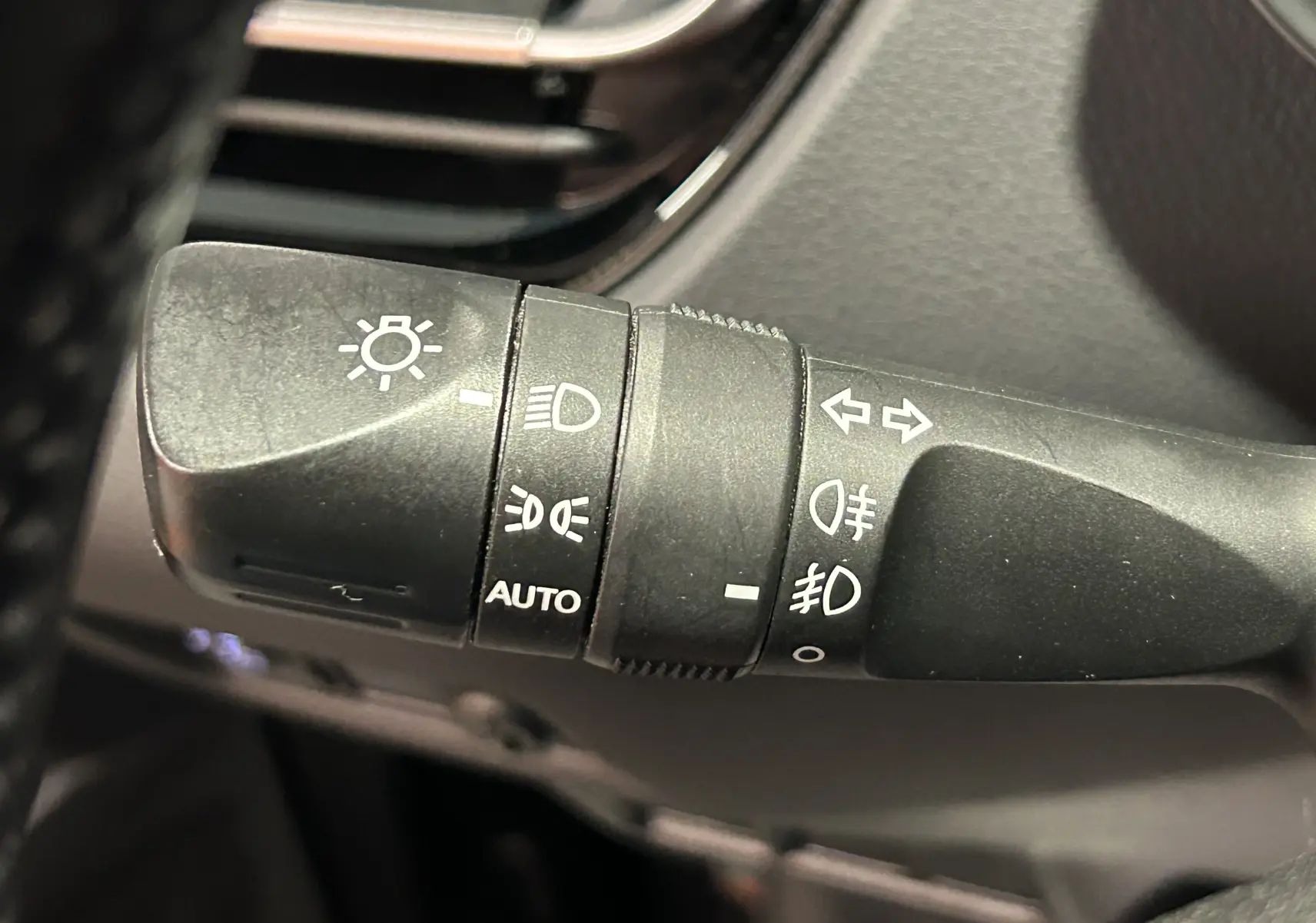 Gros plan sur la commande des phares et clignotants du Toyota C-HR Hybride 122h Edition 2WD noir métal, intérieur.