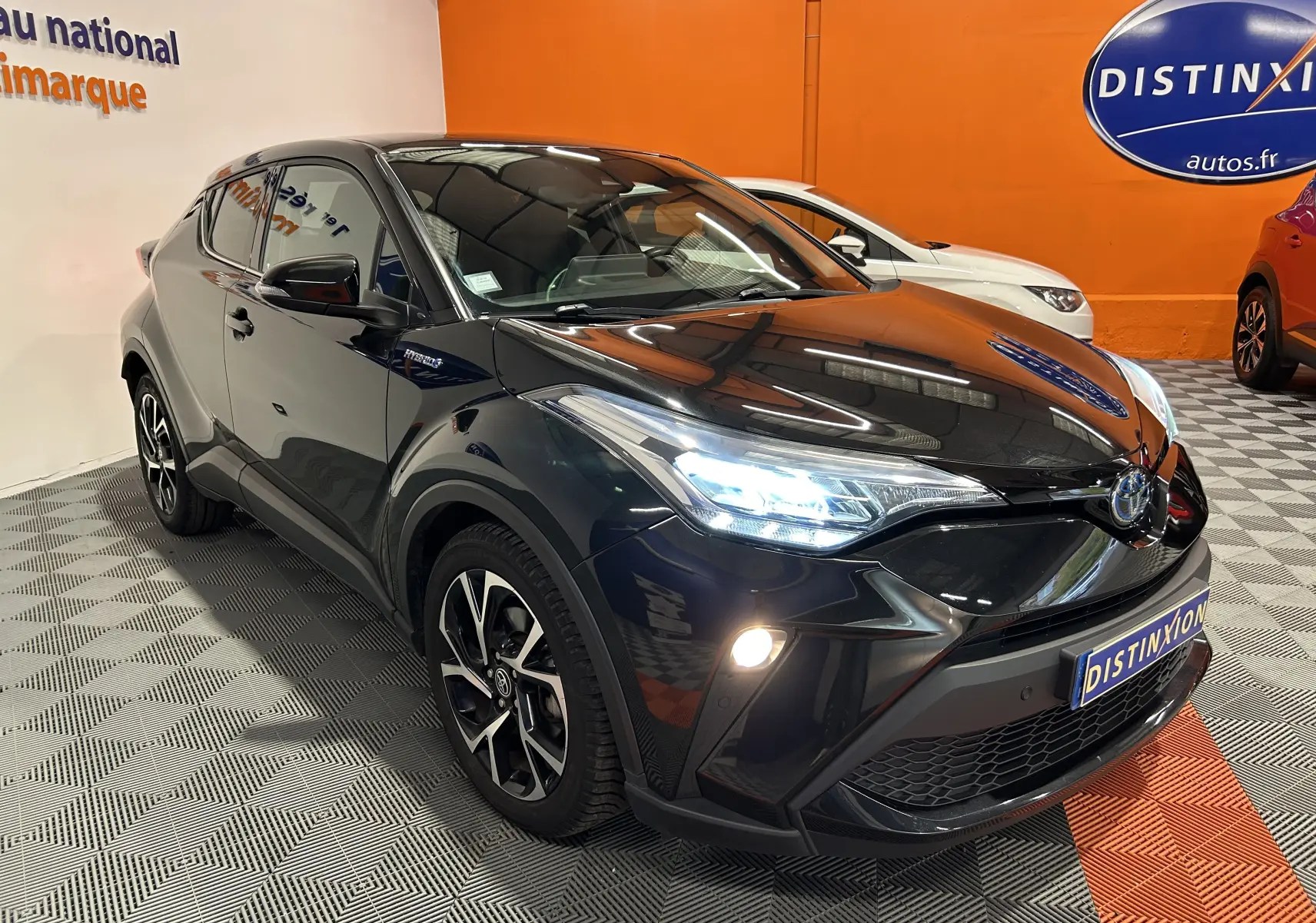 Toyota C-HR Hybride noir métal vu en 3/4 avant droit avec phares allumés dans un showroom intérieur.