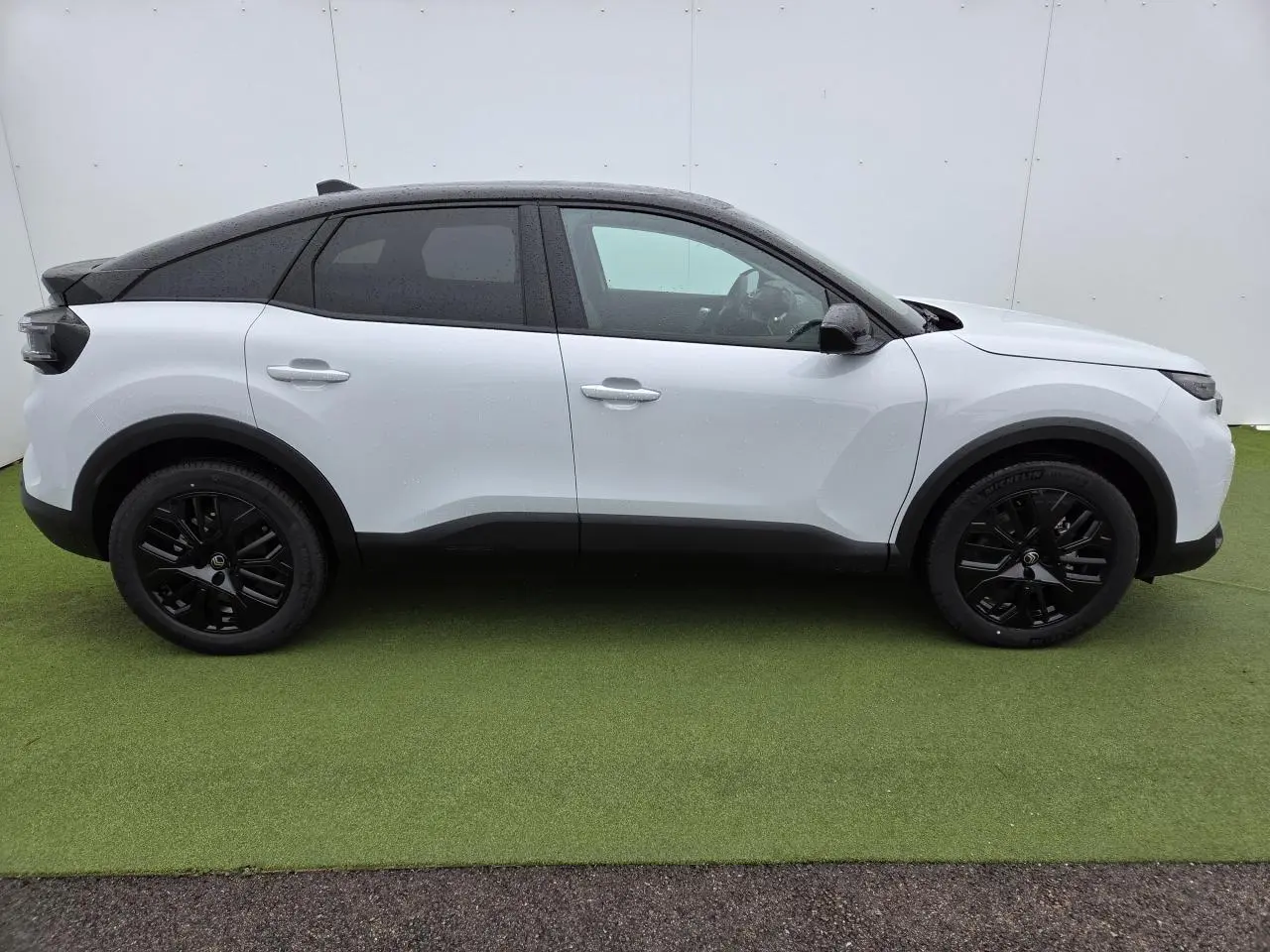 Profil côté gauche d'une Citroën C4 blanche avec toit noir et jantes alliage noires sur fond vert.