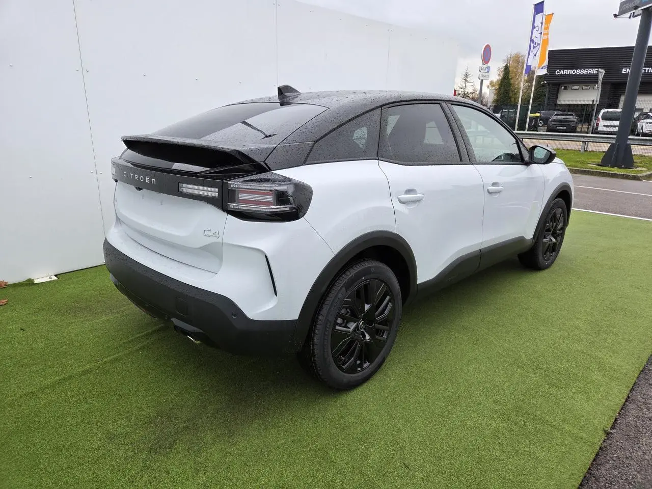 Vue 3/4 arrière droite d'une Citroën C4 blanche Okenite avec toit noir et jantes alliage noires sur pelouse verte.