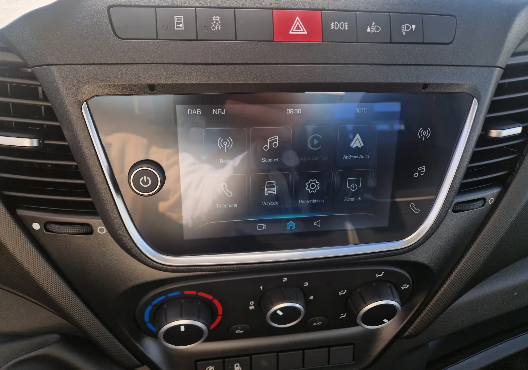 Vue intérieure côté conducteur de la cabine blanche de l’Iveco Daily Châssis Cabine avec sièges noirs et tableau de bord visible.