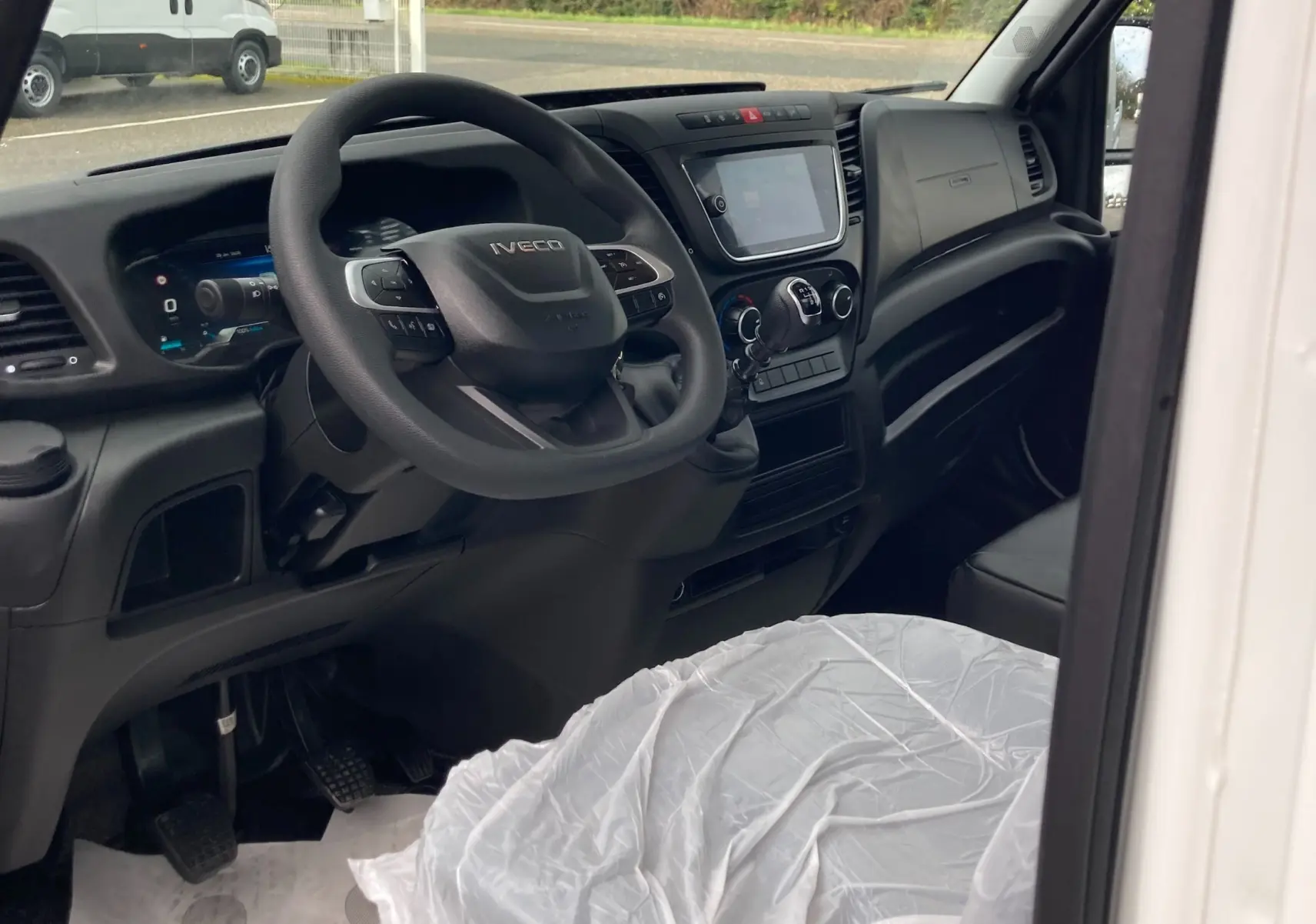 Vue intérieure côté conducteur de l'Iveco Daily blanc, montrant le volant, tableau de bord et levier de vitesses manuel.