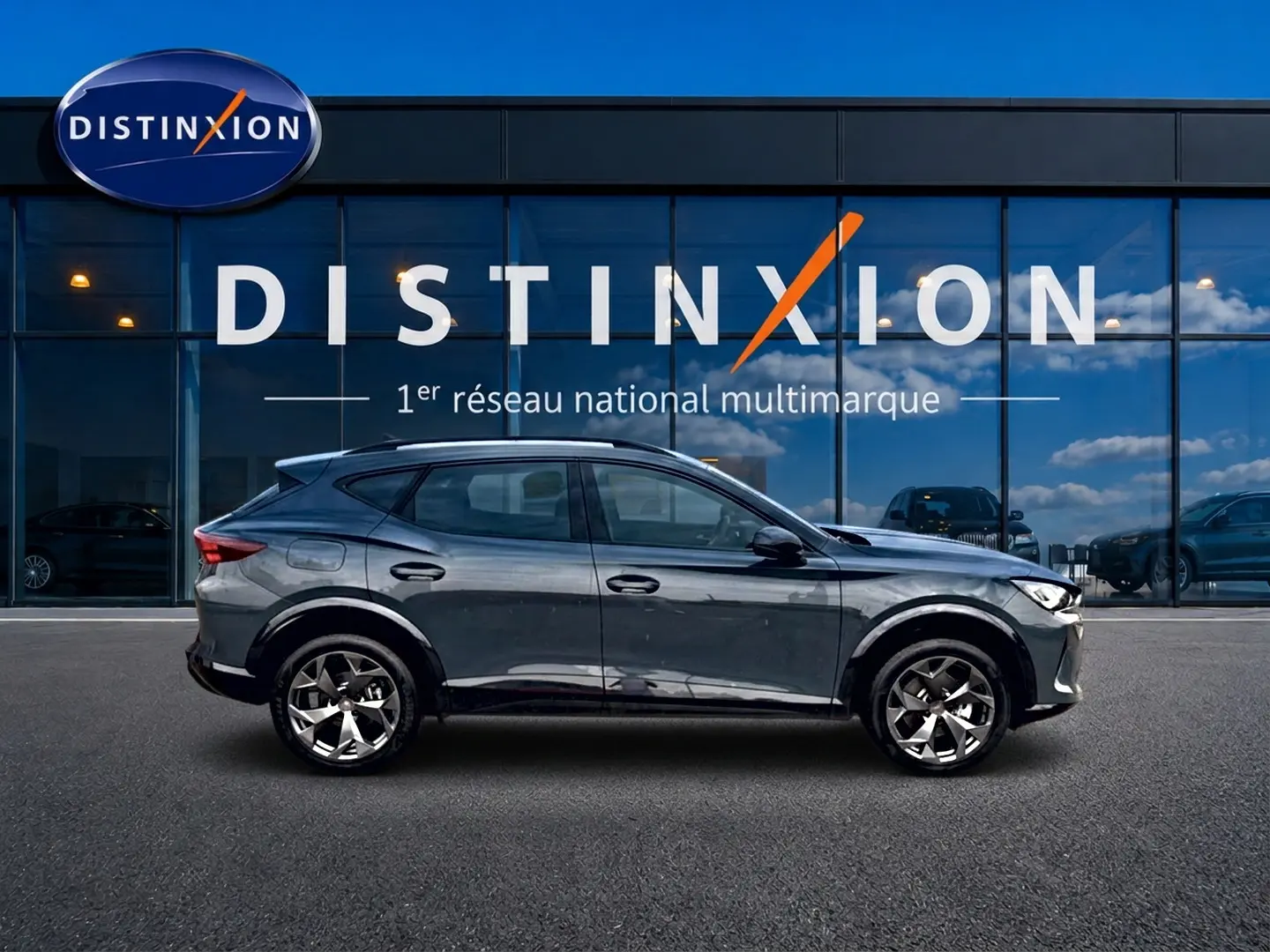 Profil côté gauche d'un CUPRA Formentor 1.5 etsi hybrid 2026 en bleu fjord avec jantes 18 pouces devant une vitrine Distinxion.