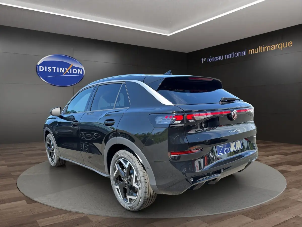 Volkswagen T-Roc noir vu en 3/4 arrière droit, avec feux LED et attelage visible en showroom.