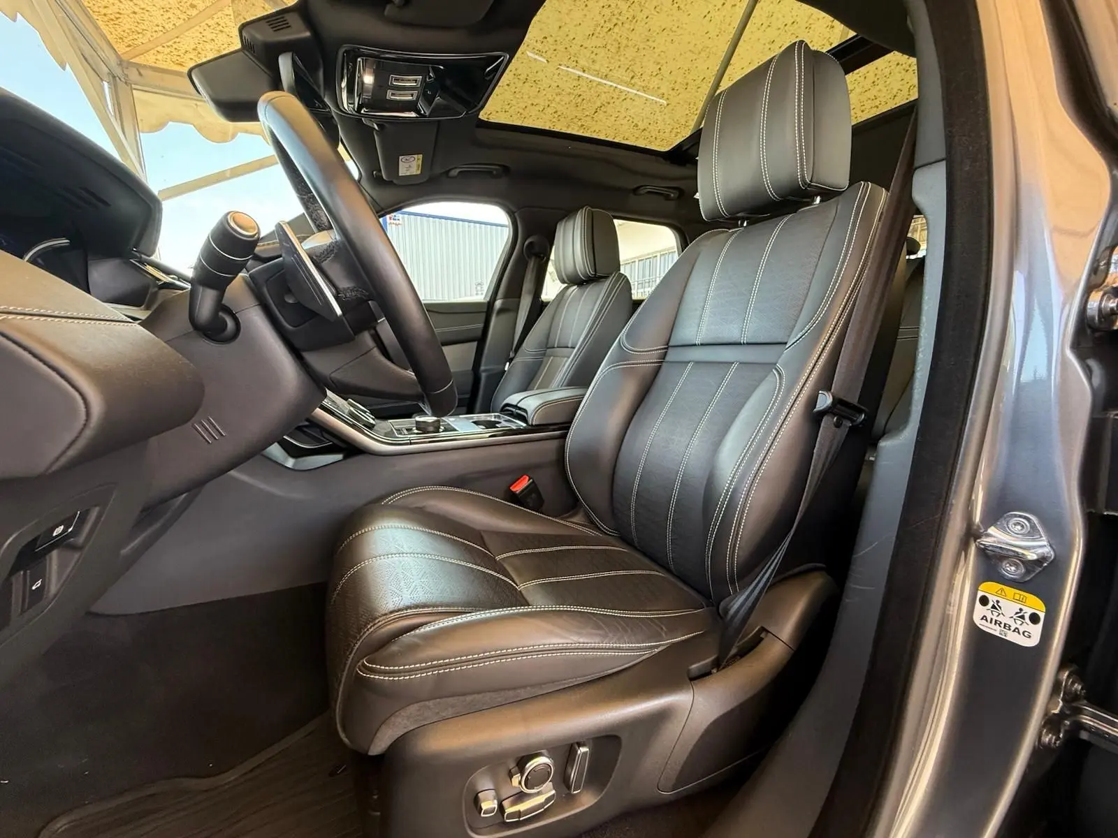 Vue intérieure côté conducteur du Range Rover Velar gris 2019, mettant en valeur les sièges cuir Windsor et le volant multifonction.