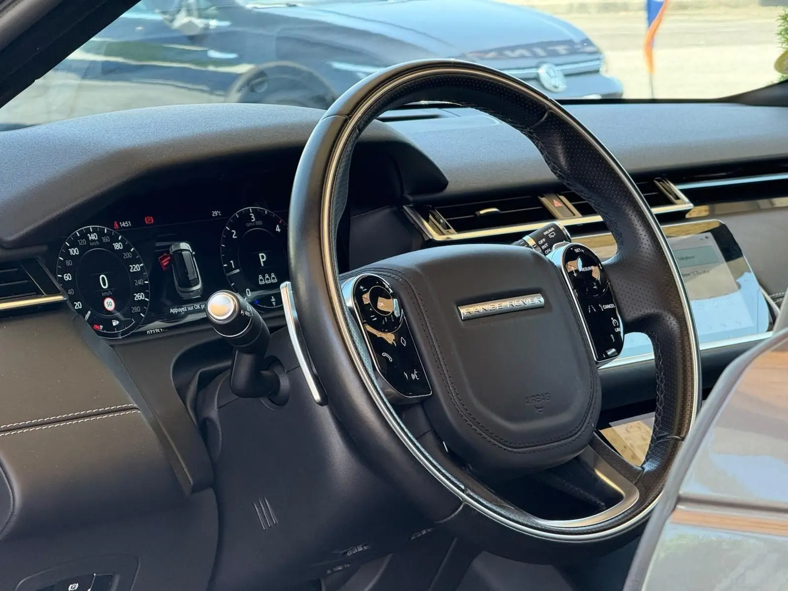Vue rapprochée du volant en cuir noir du Range Rover Velar 2019 avec tableau de bord numérique et écran tactile.