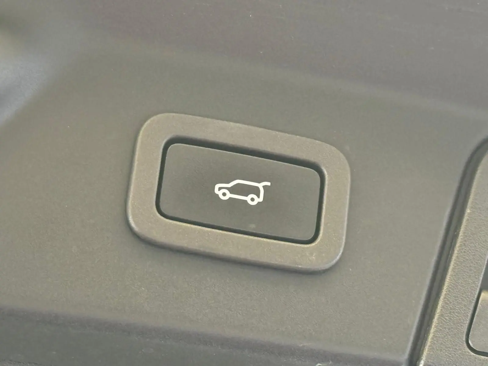 Bouton noir avec pictogramme d'ouverture du hayon, situé à l'intérieur du Range Rover Velar gris 2019.