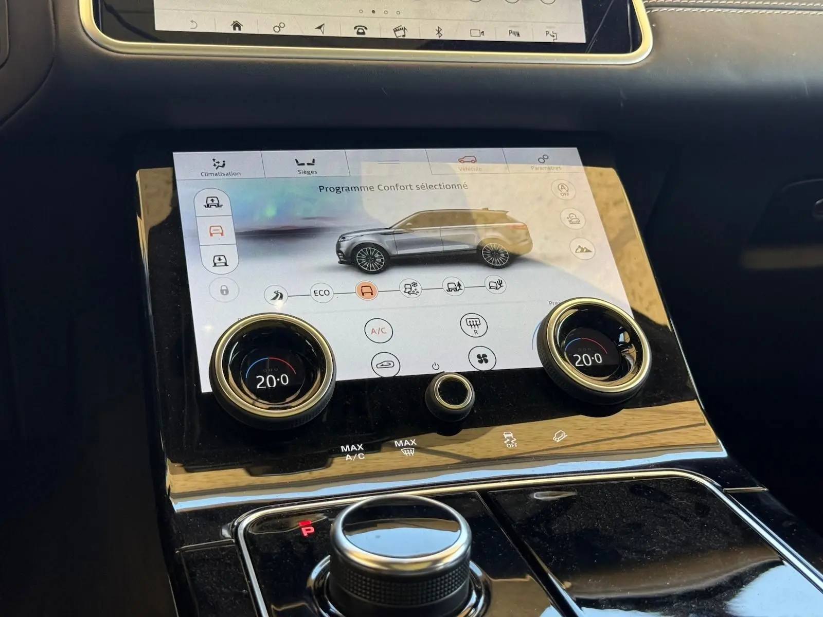 Vue rapprochée de la console centrale du Range Rover Velar gris, avec écran tactile et commandes de climatisation digitales.