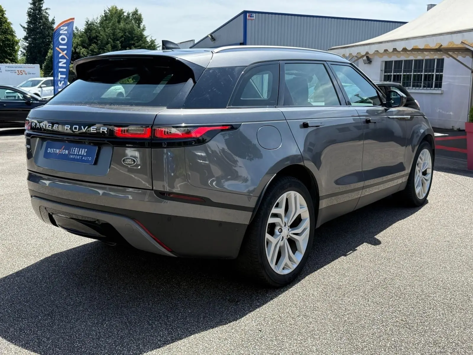 Range Rover Velar gris en 3/4 arrière droit, avec feux LED fins et jantes alliage blanches visibles.