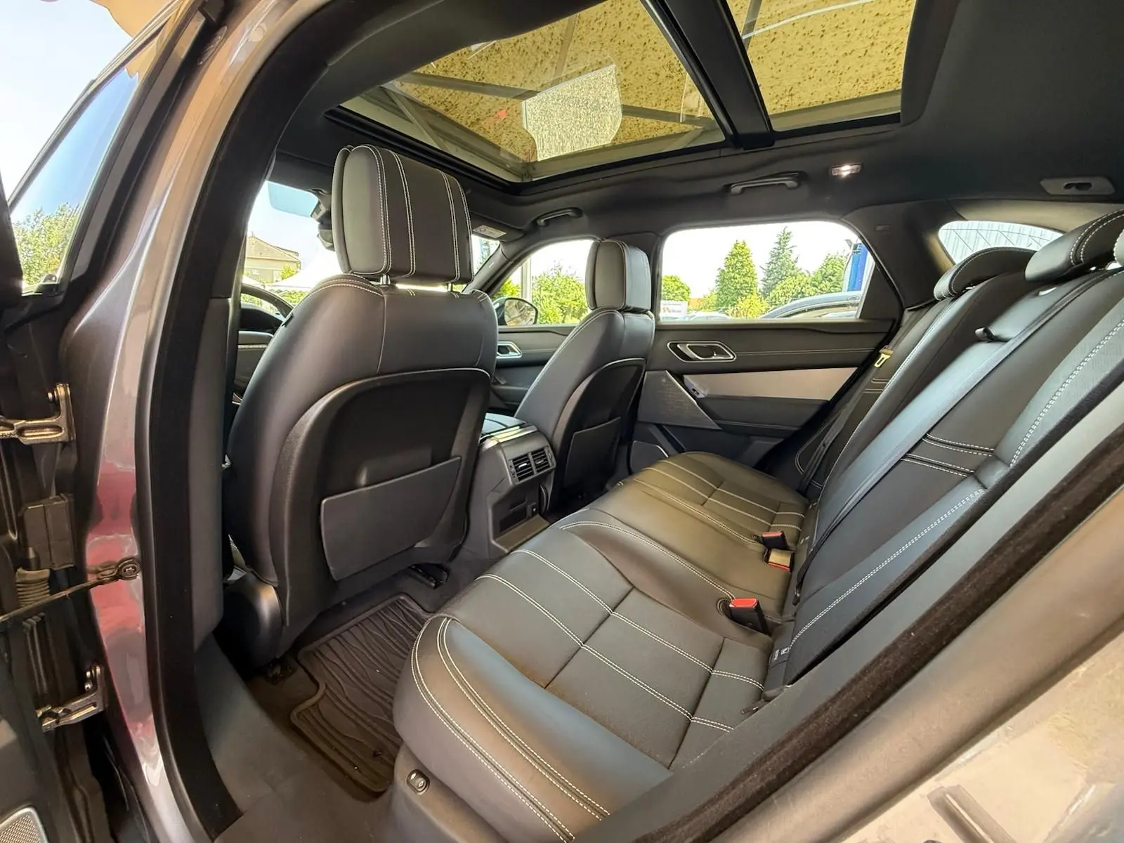Intérieur arrière du Range Rover Velar gris 2019, vue côté gauche avec sièges cuir noirs et toit panoramique.