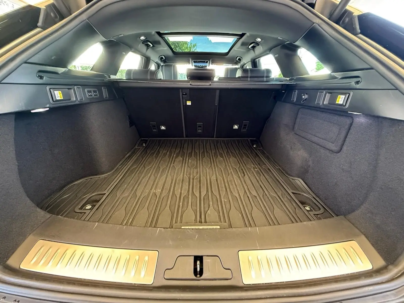 Coffre spacieux du Range Rover Velar gris 2019 vu de l'arrière avec plancher caoutchouc et toit panoramique.