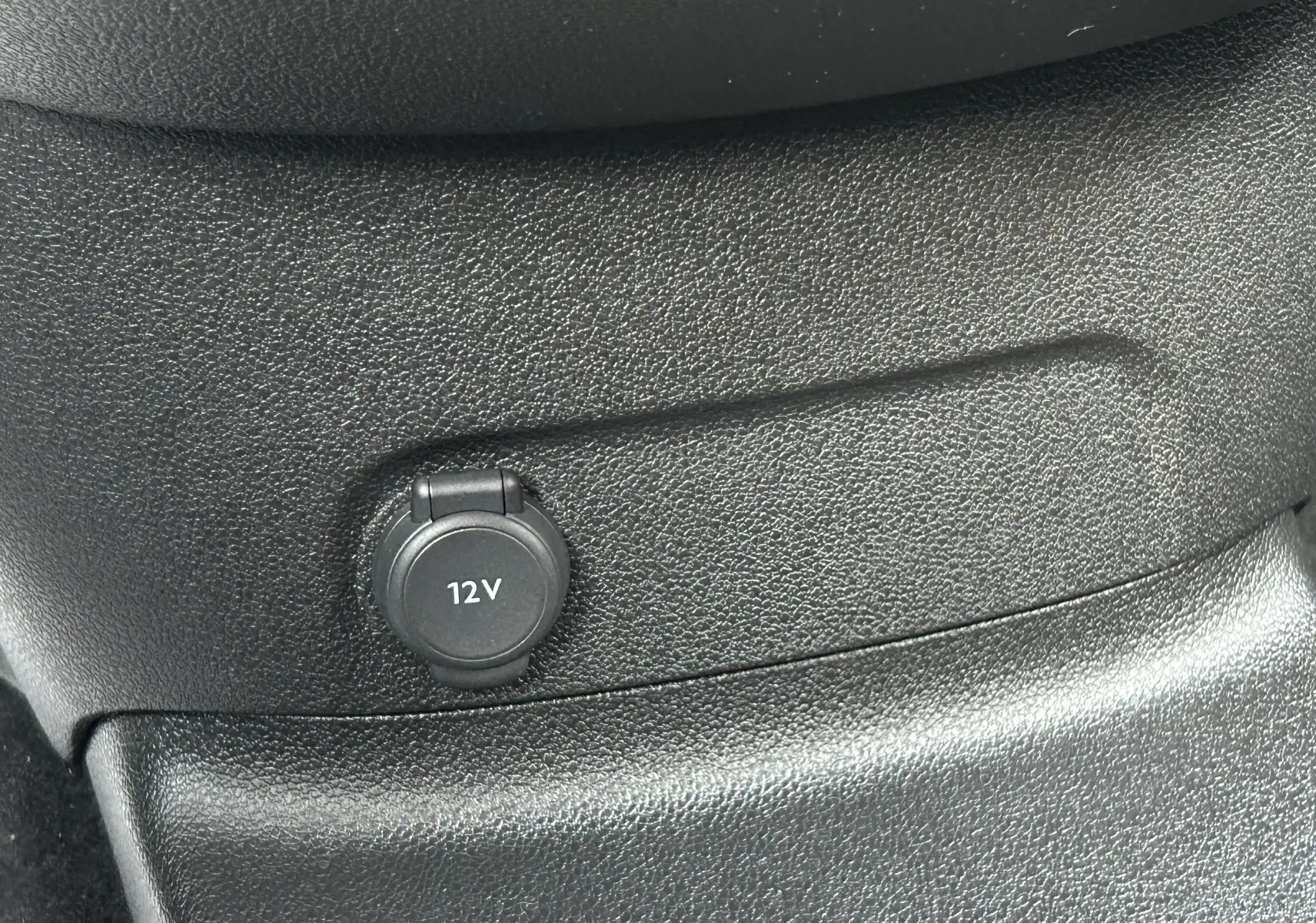 Prise 12V intégrée dans la console centrale noire du Peugeot Partner Fourgon blanc, vue intérieure rapprochée.