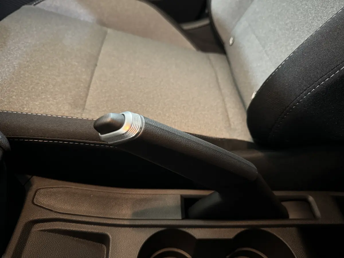 Le frein à main manuel en gros plan entre les sièges avant gris clair de la Renault Clio 2025 Evolution Blue dCi 100.