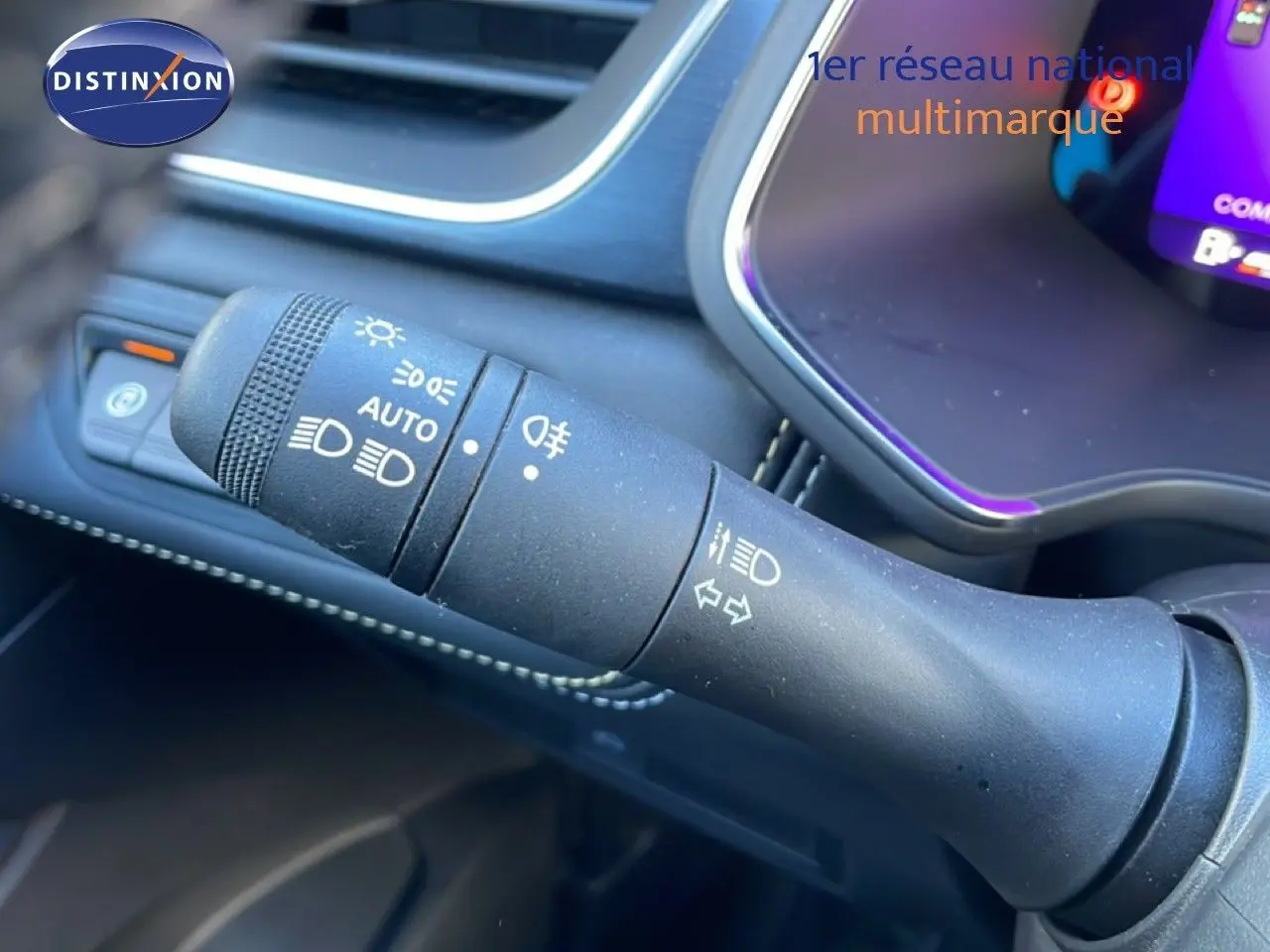 Gros plan sur la commande des phares et clignotants dans l'habitacle du Renault Symbioz bleu Iron Metal, tableau de bord partiellement visible.