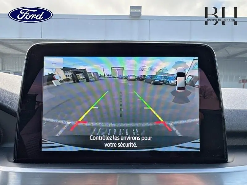 Écran tactile affichant la caméra de recul du Ford Kuga noir Agate, vue arrière avec repères de stationnement colorés.