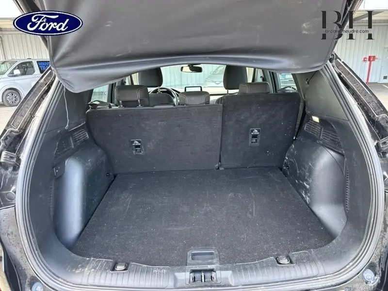 Coffre ouvert vu de l'arrière d'un Ford Kuga noir Agate Métallisée avec banquette arrière partiellement rabattue.