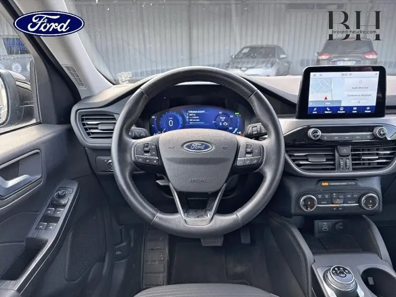 Vue intérieure frontale du tableau de bord du Ford Kuga 2023 noir, avec volant cuir multifonction et écran tactile GPS.