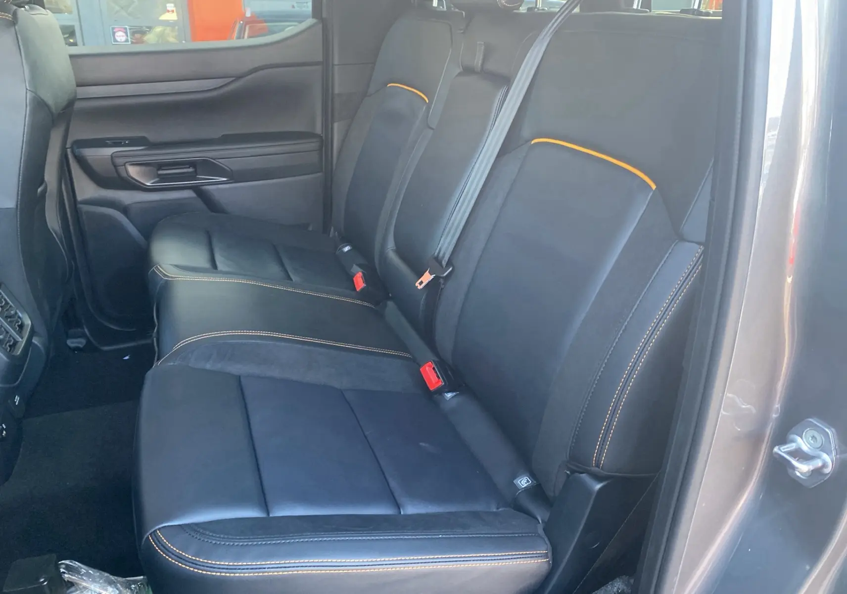 Vue intérieure côté droit des sièges arrière noirs avec surpiqûres orange du Ford Ranger gris carbone 2026 Wildtrak X Pack.
