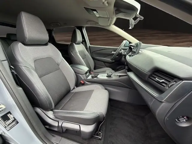 Vue intérieure côté conducteur du Nissan Qashqai 2025 gris foncé, montrant les sièges tissu et le tableau de bord moderne.