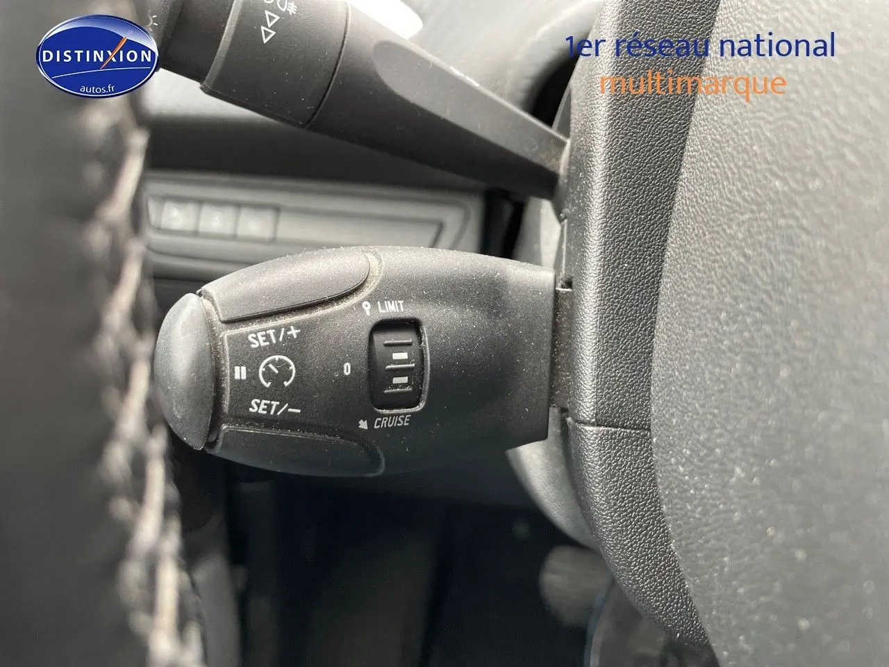 Gros plan sur la commande de régulateur de vitesse à gauche du volant d'un Peugeot 2008 blanc nacré de 2015.