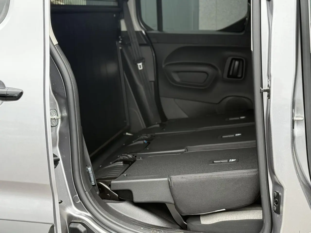 Vue intérieure côté droit du Citroën Berlingo Multispace gris acier avec sièges arrière rabattus et porte coulissante ouverte.