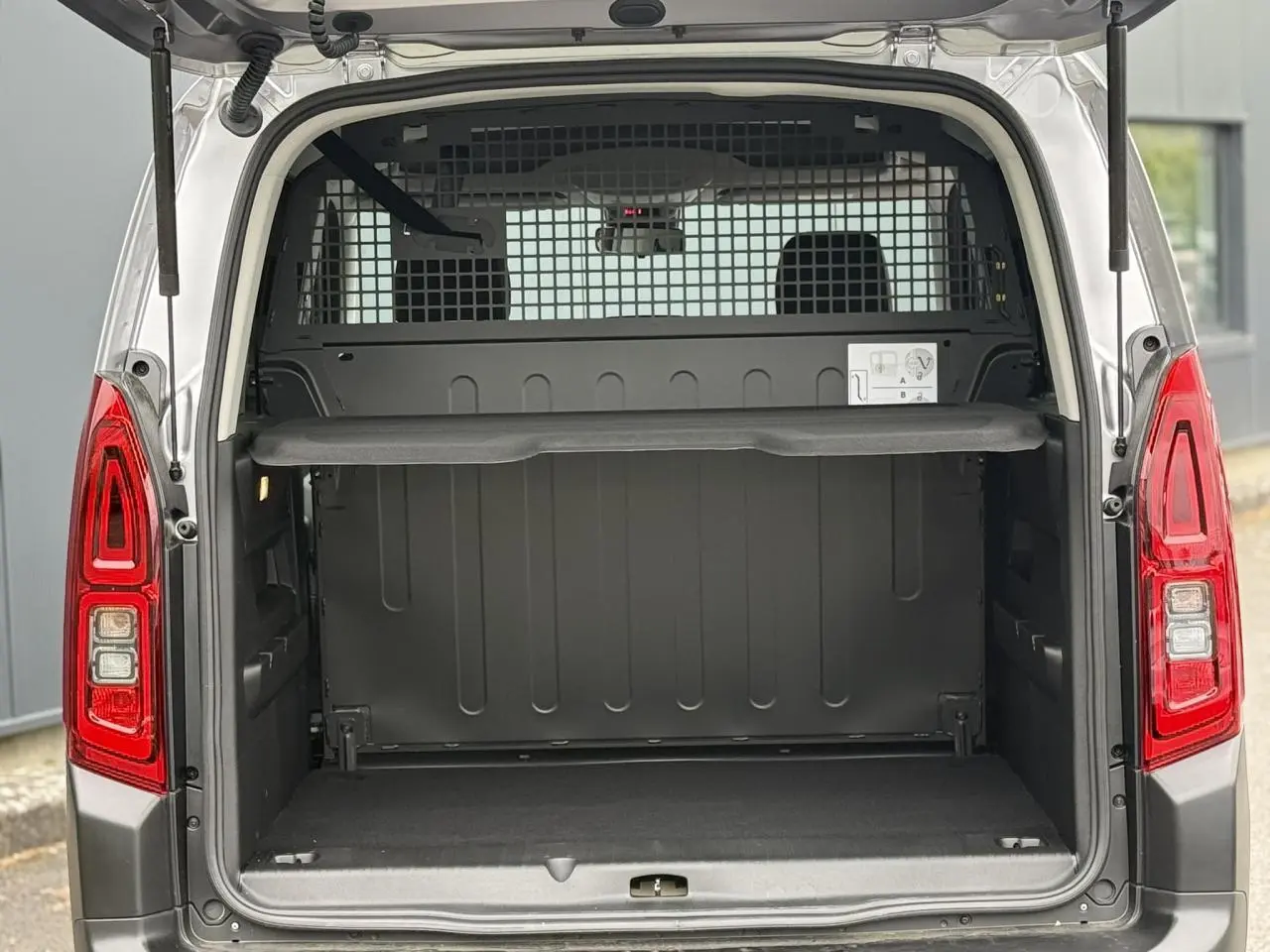 Coffre ouvert vu de l'arrière d'un Citroën Berlingo Multispace gris acier avec lunette arrière ouvrante et séparation grillagée.