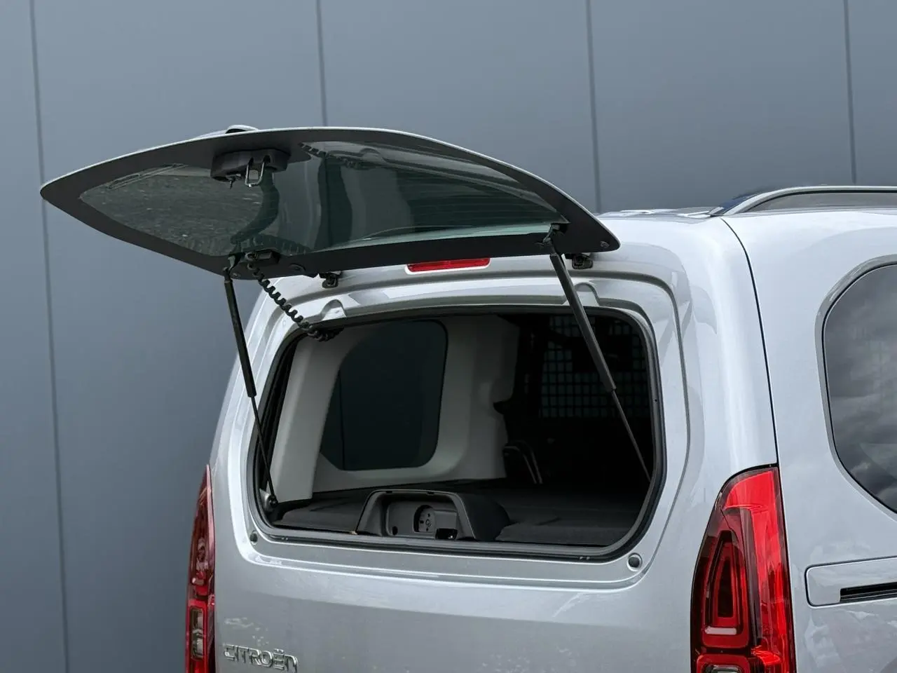 Vue arrière du Citroën Berlingo gris acier avec lunette arrière ouvrante relevée et intérieur partiellement visible.
