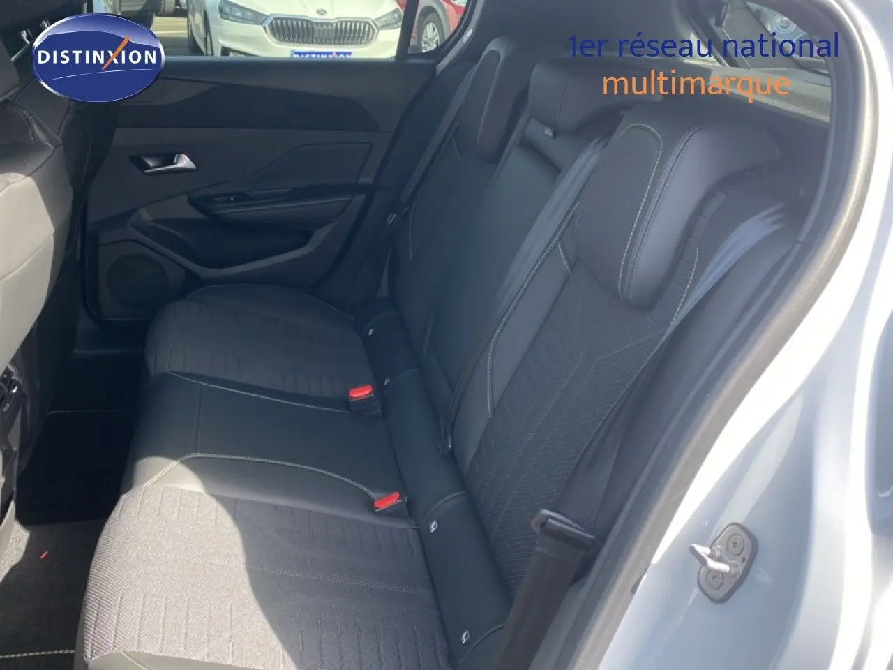 Vue côté droit sur l'intérieur arrière d'une Peugeot 308 blanche, sièges noirs en tissu et cuir avec surpiqûres contrastantes.