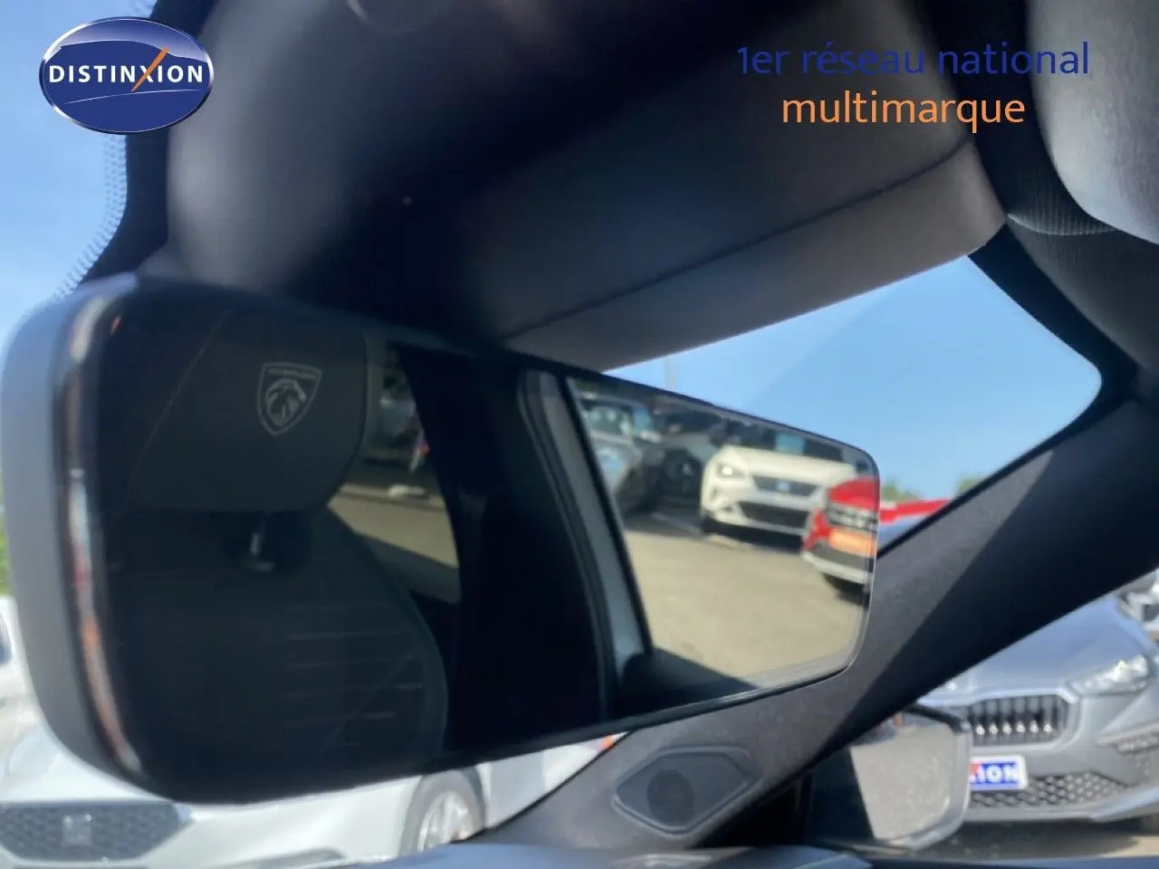 Rétroviseur intérieur reflétant le siège avant gauche avec logo Peugeot, vue partielle du blanc Okenite métal extérieur.
