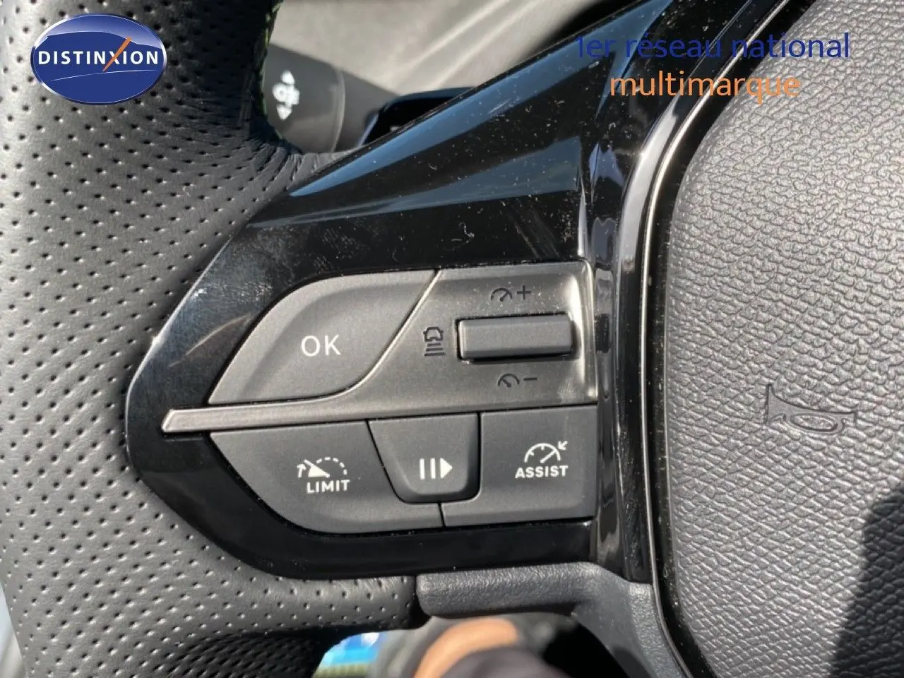 Gros plan sur les commandes gauche du volant perforé noir d’une Peugeot 308 hybride blanche, avec boutons de régulateur et assistant.