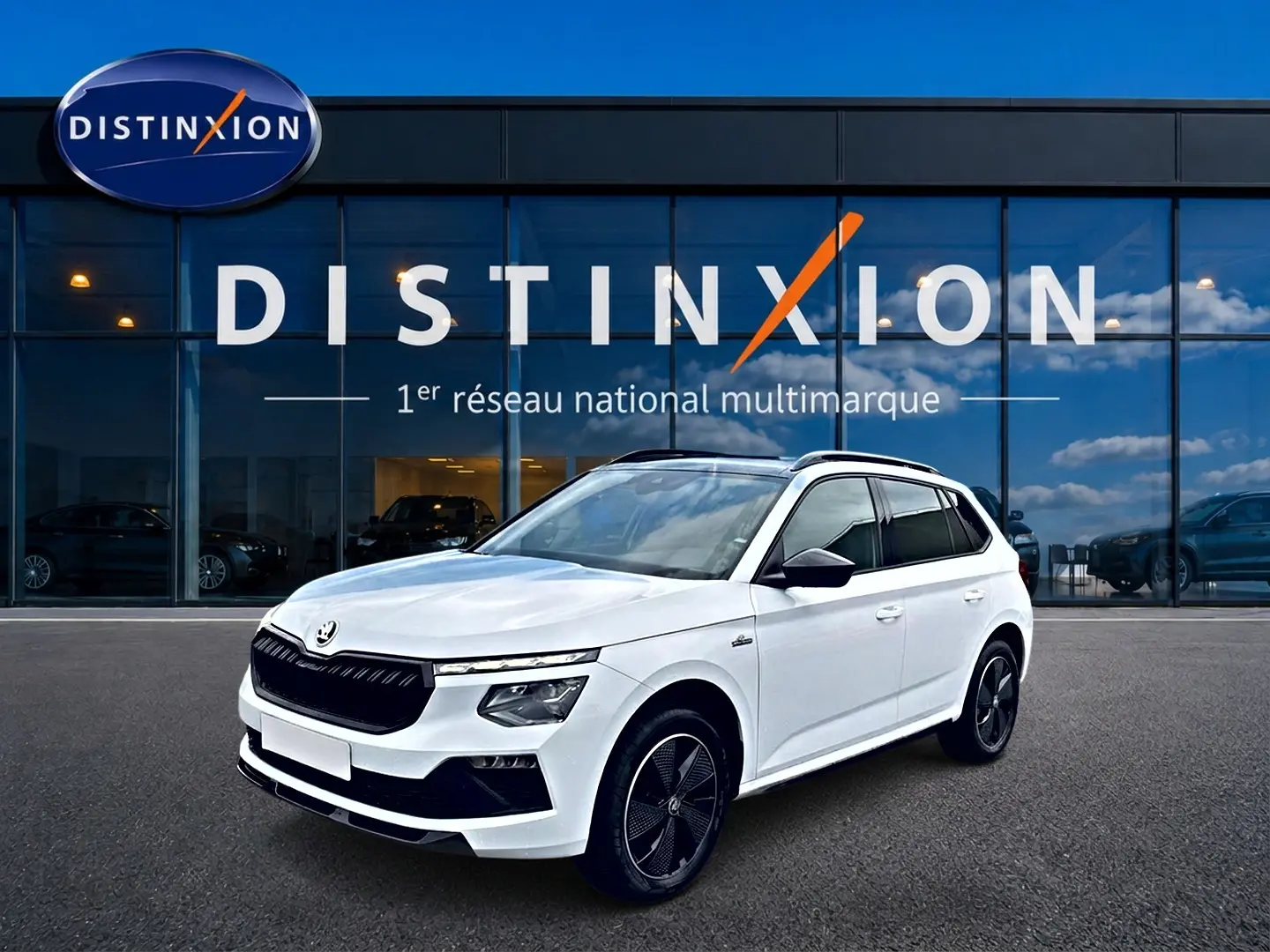 Vue 3/4 avant d'un Skoda Kamiq blanc nacré avec jantes noires et toit panoramique devant une vitrine Distinxion.