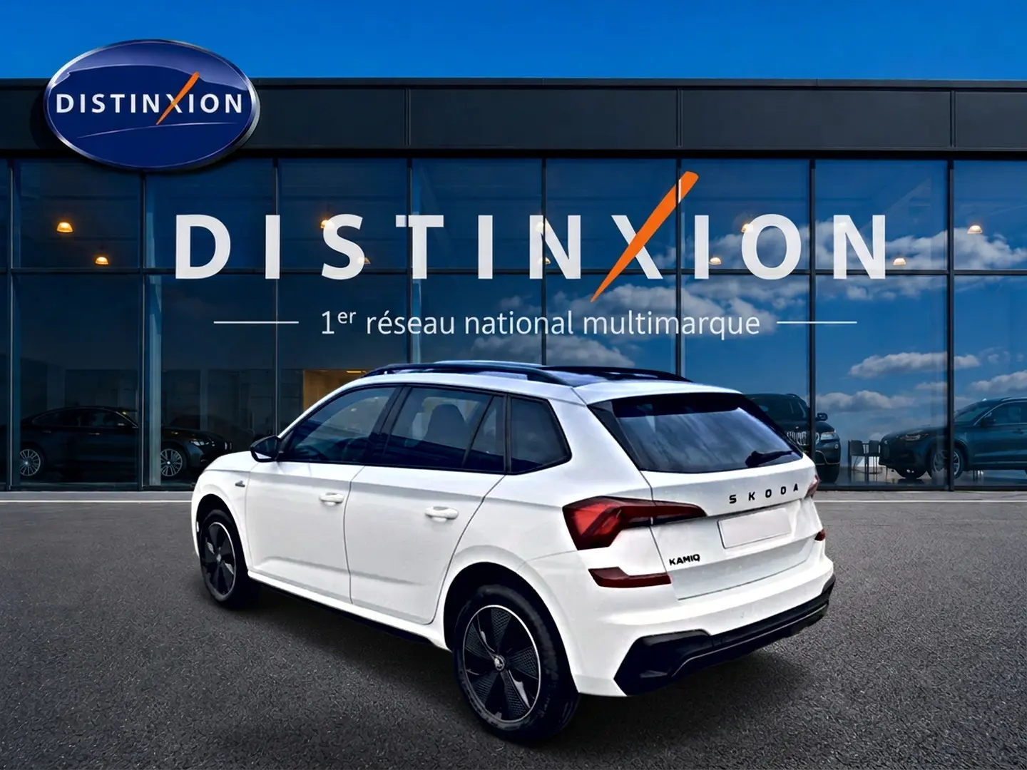 Vue 3/4 arrière droite d'un Skoda Kamiq blanc nacré avec jantes noires et toit panoramique, devant une vitrine Distinxion.