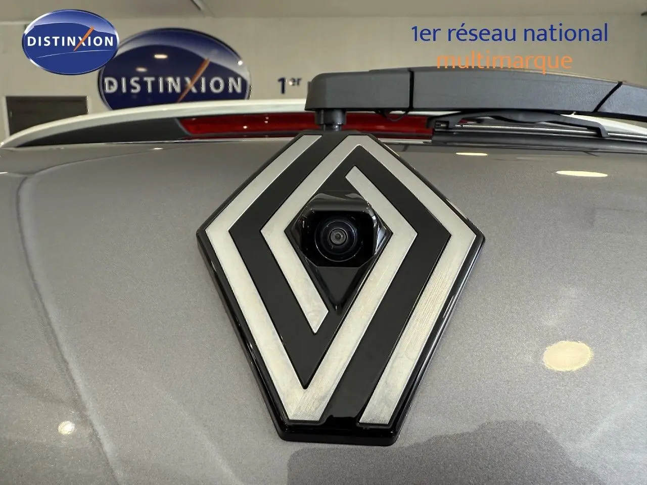 Gros plan sur le logo Renault gris métallisé avec caméra intégrée, sur le capot gris Cassiopée du Captur 2025.