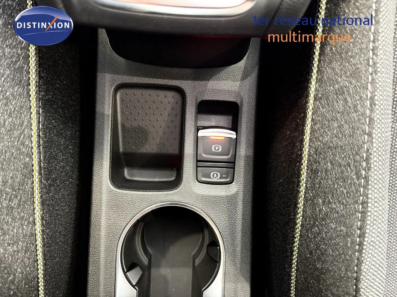 Gros plan sur la console centrale du Renault Captur gris cassiopée, avec bouton frein à main électrique et tissu gris à surpiqûres jaunes.