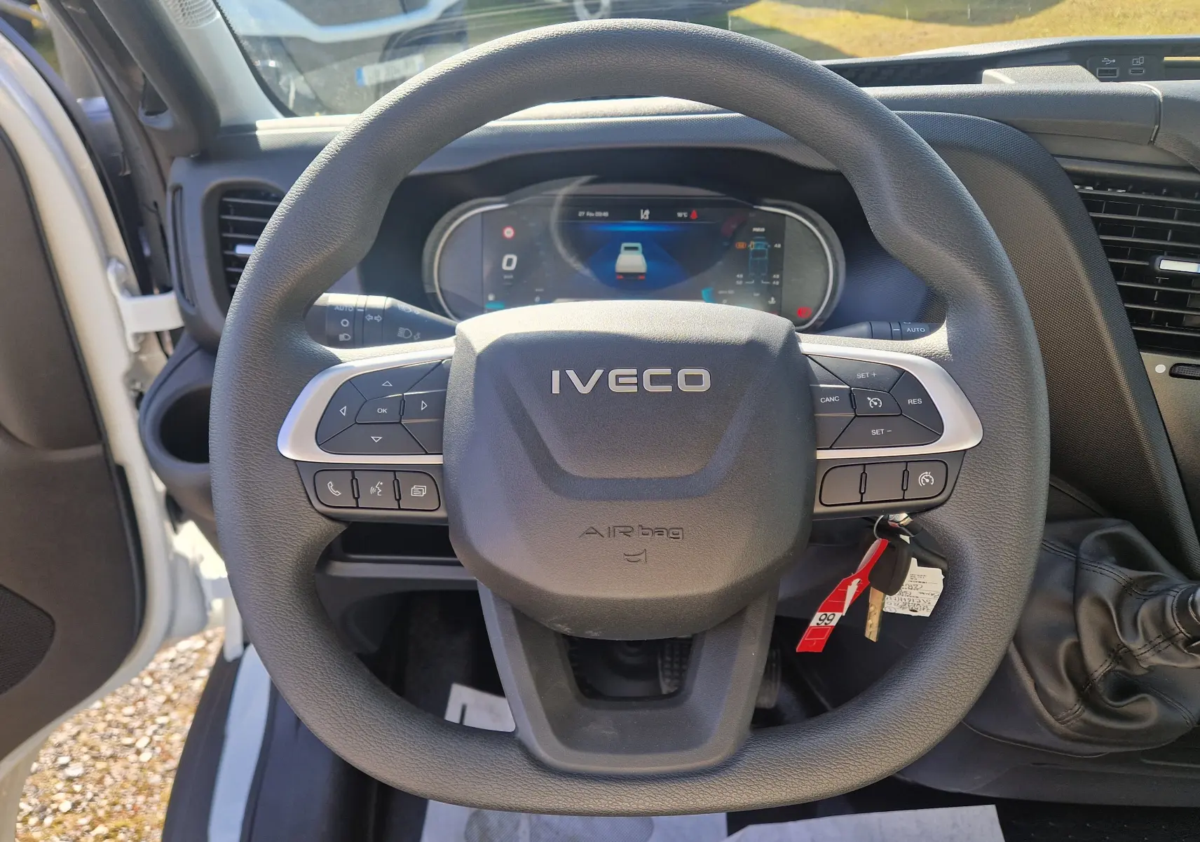Vue intérieure centrée sur le volant IVECO noir du Daily Chassis Cabine blanc avec tableau de bord digital en arrière-plan.