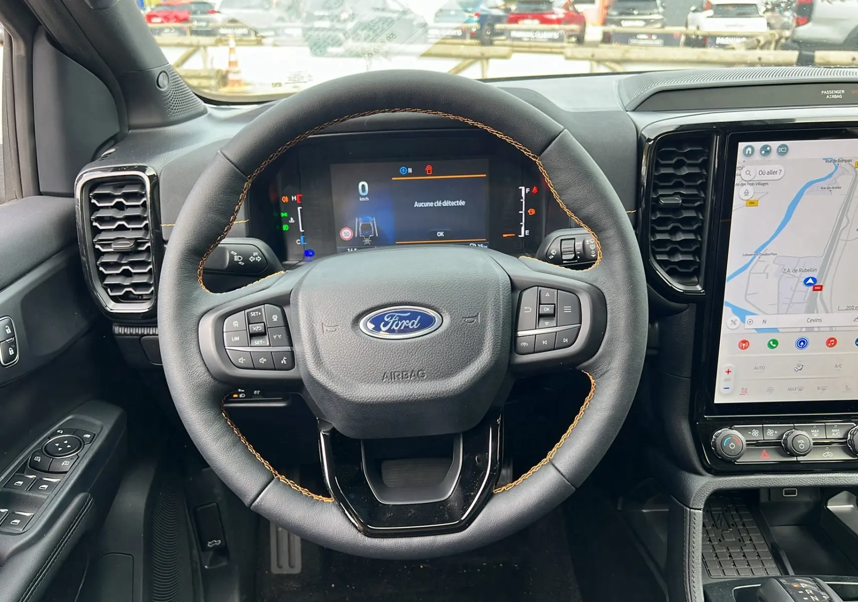 Vue intérieure centrée sur le volant cuir noir avec surpiqûres orange du Ford Ranger 2025, tableau de bord et écran tactile visibles.