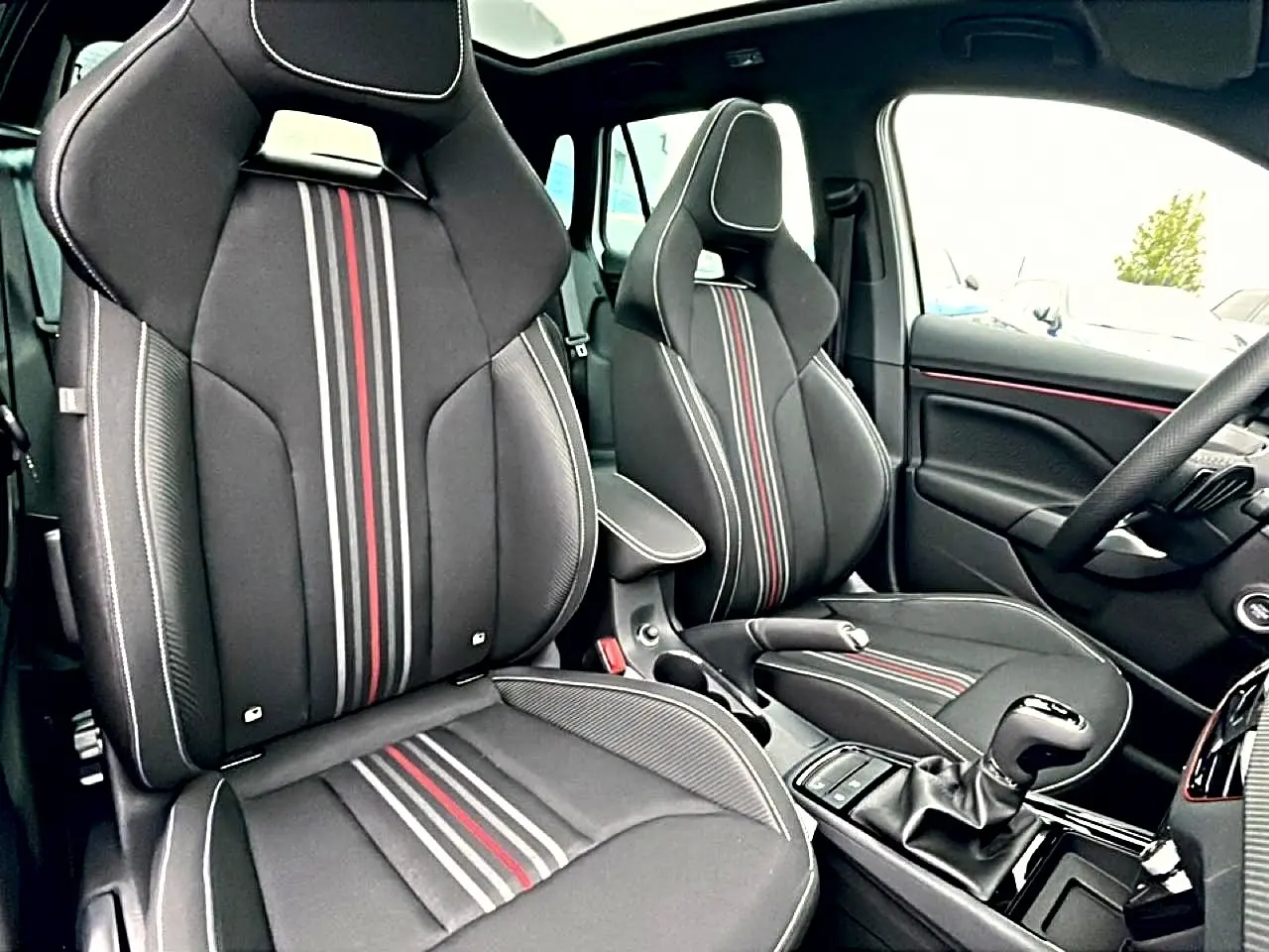 Vue intérieure avant du Skoda Kamiq Monte Carlo 2026, sièges sport noirs avec bandes rouges et grises centrales.