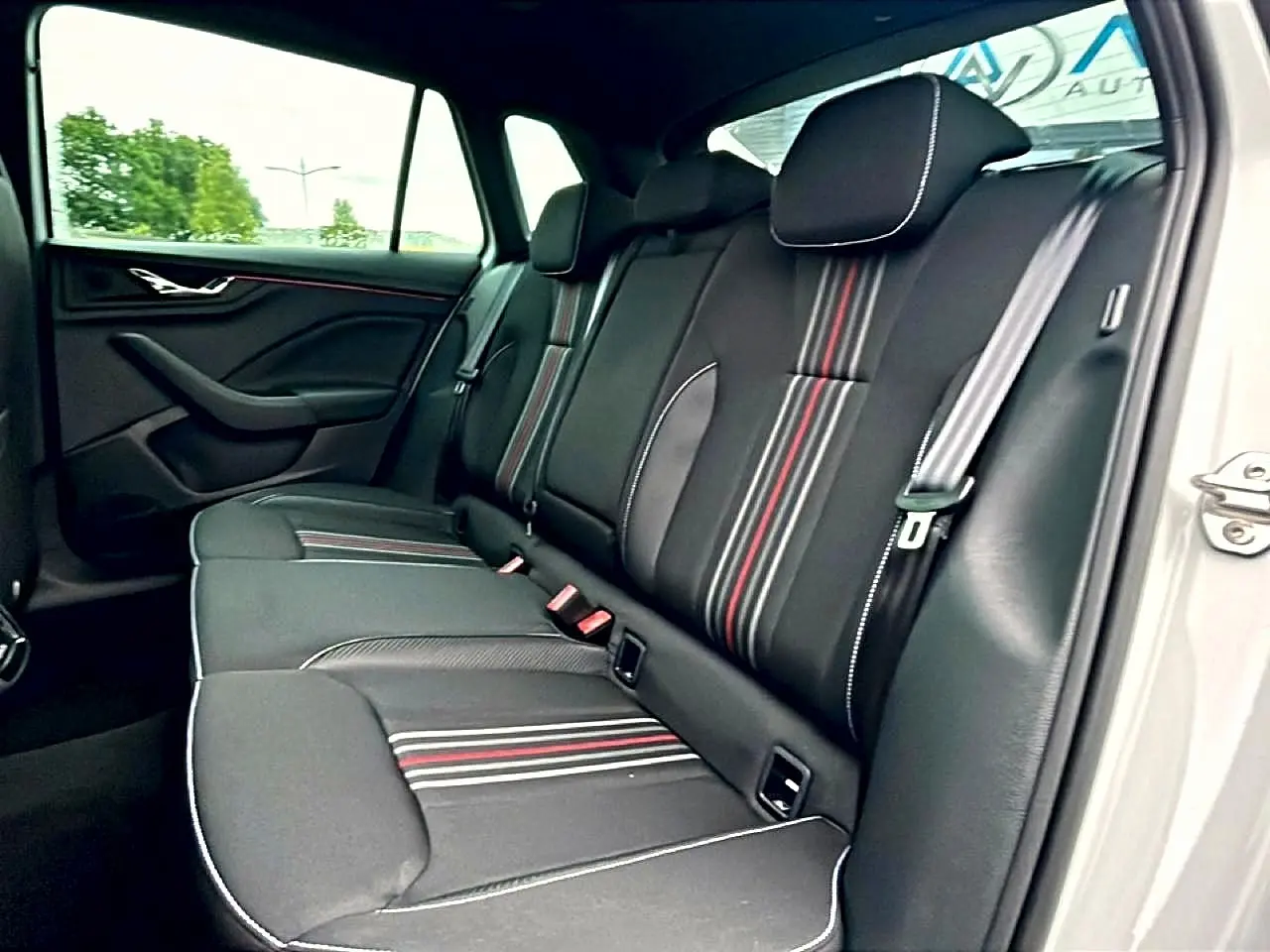 Vue intérieure côté droit sur la banquette arrière noire avec surpiqûres blanches et bandes rouges du Skoda Kamiq blanc nacré.