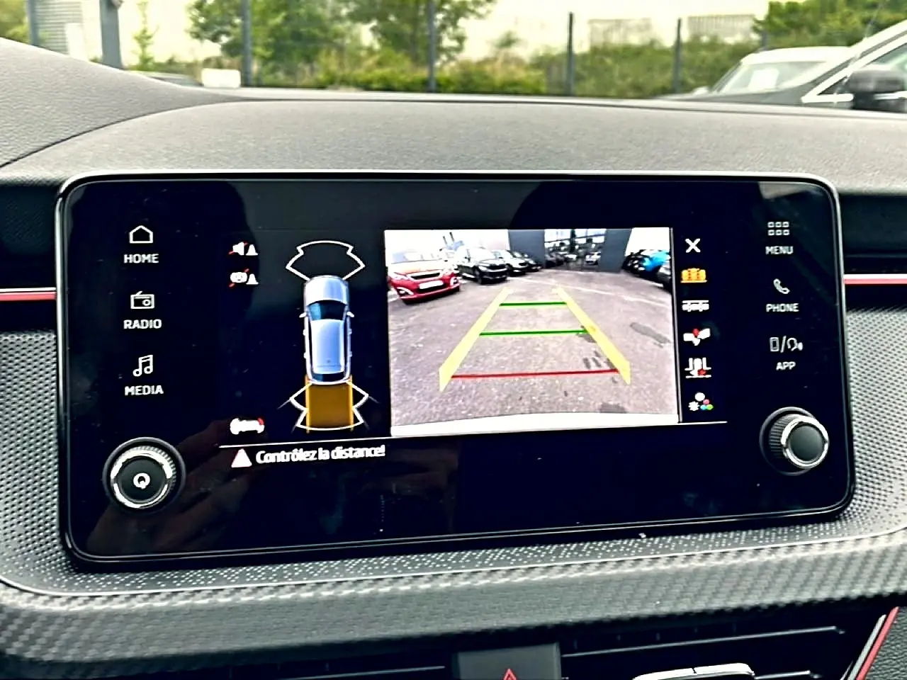Écran tactile du tableau de bord du Skoda Kamiq blanc nacré montrant la caméra de recul et l’aide au stationnement.