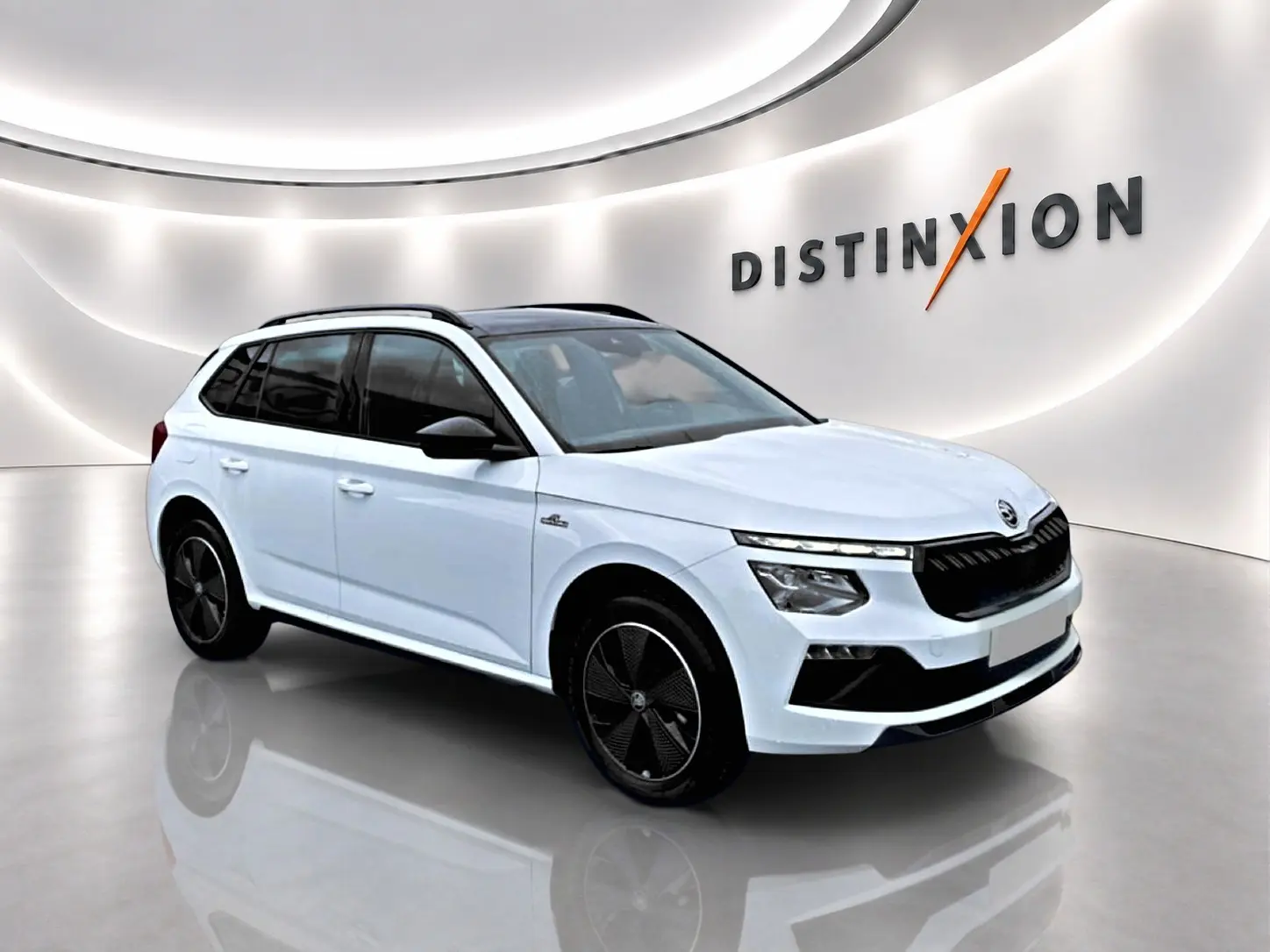 Vue 3/4 avant droite d'un Skoda Kamiq blanc nacré avec jantes noires et toit panoramique en showroom lumineux.