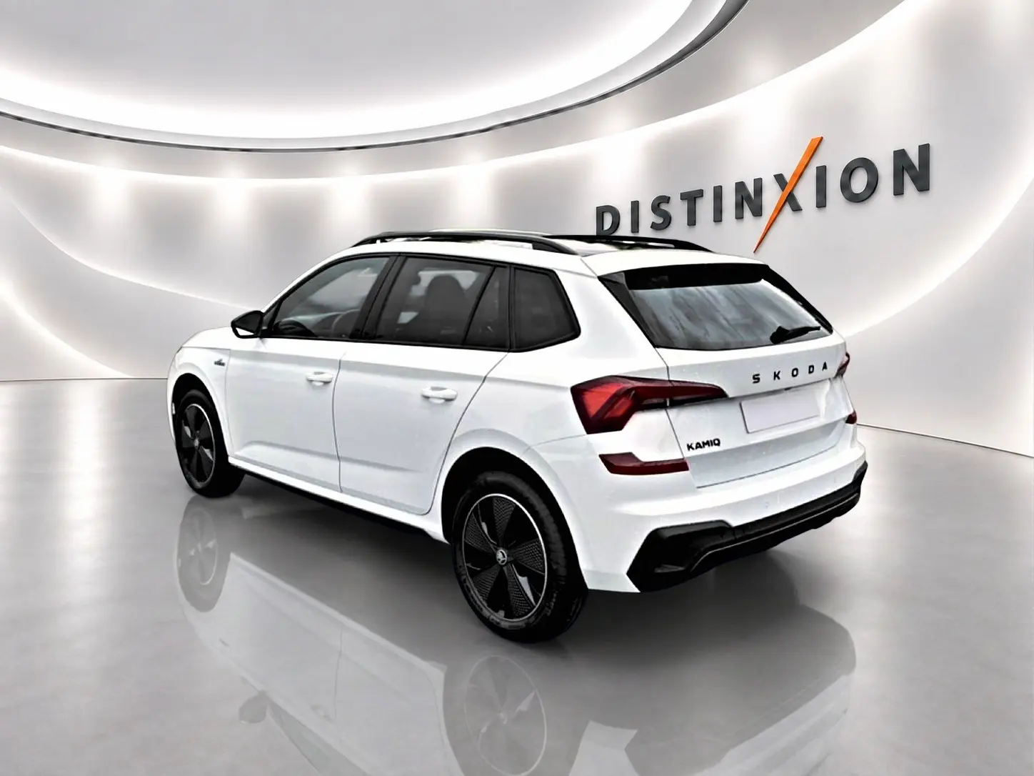 Vue 3/4 arrière droite d'un Skoda Kamiq blanc nacré avec jantes noires dans un showroom lumineux.
